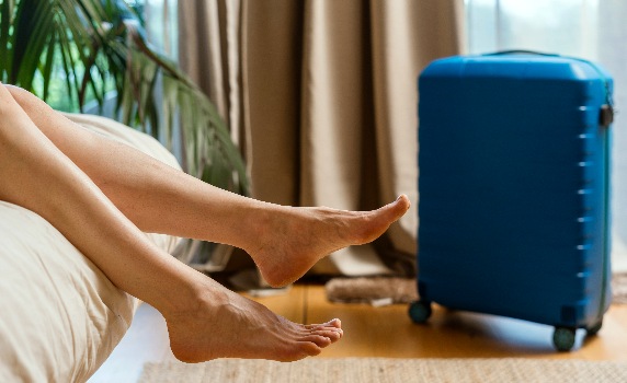 Bare-feet-dangling-off-bed-by-suitcase