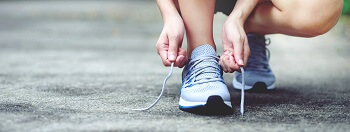 Person tying supportive running shoes before exercising to ensure proper fit and prevent foot injuries.