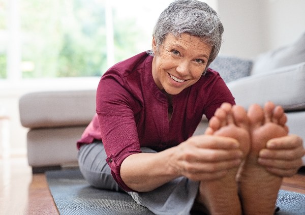 Smiling-woman-bent-over-legs-holding-healthy-feet