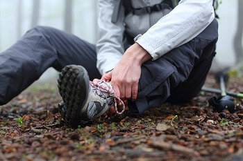 Hiker holding injured ankle after twisting foot on trail