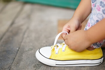 Child tying yellow sneakers with proper shoe fit.