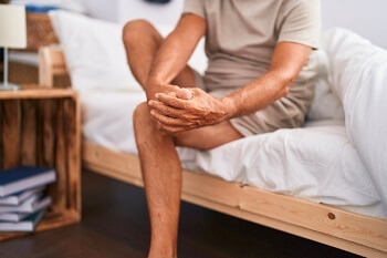 man sitting on the edge of a bed massaging his foot and ankle to relieve morning foot pain
