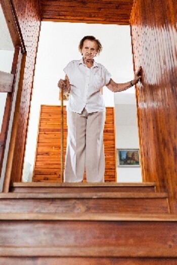Senior woman using a cane while descending wooden stairs, demonstrating fall-risk concerns